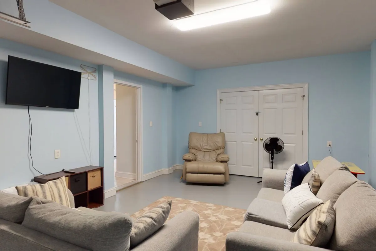 A comfortable living space featuring two sofas, a recliner, a large television, and open doorways to adjoining rooms. The room is arranged for relaxation and social activities, with plenty of seating and a welcoming atmosphere for families.