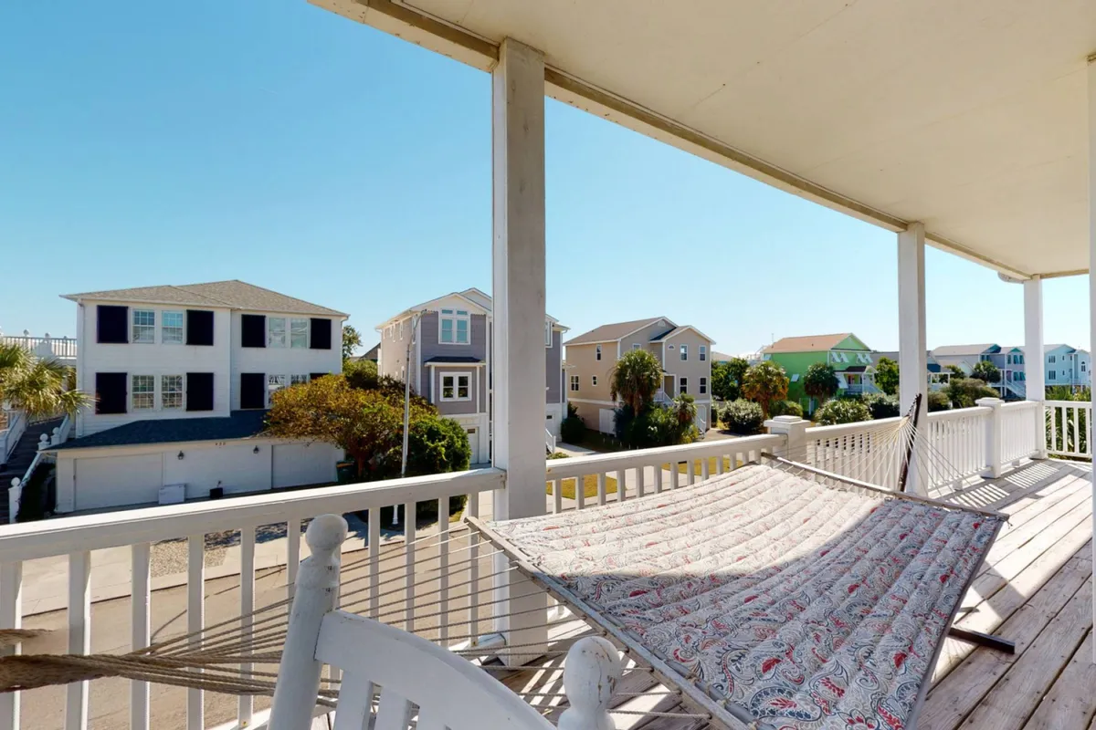 A tranquil porch setup featuring a hammock, neighboring houses, and a clear blue sky. The hammock invites relaxation while the porch offers a shaded retreat, evoking the ease of outdoor living.