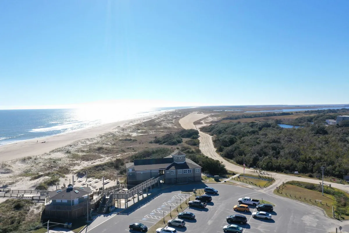 A scenic exterior shot featuring a beachfront area with a pathway, dunes, and water views. There is a sense of peacefulness, emphasizing the inviting walking paths and the natural beauty of the local environment, suggesting easy access for dog walks and exploration.
