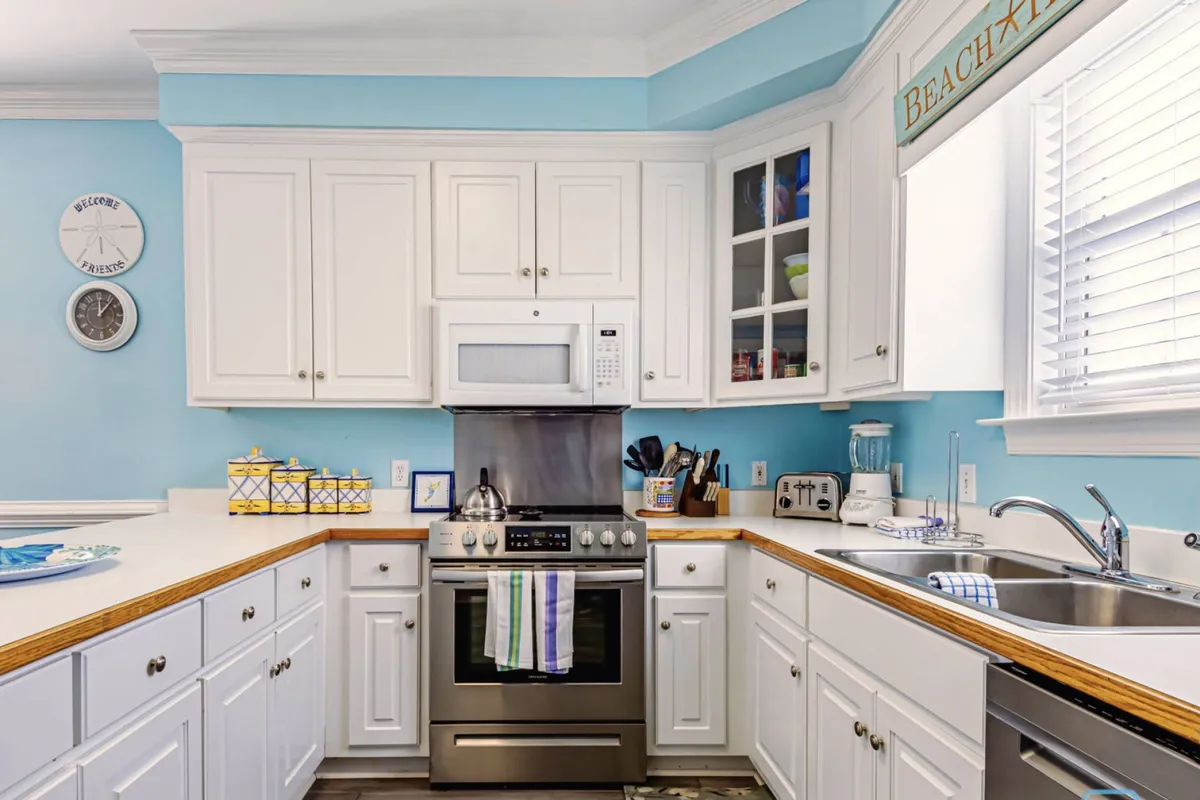 A bright, cheerful kitchen with white cabinetry, stainless steel appliances, and blue accents. The space is set up for cooking and family meals, reinforcing the section’s mention of preparing fresh seafood and enjoying time together indoors.
