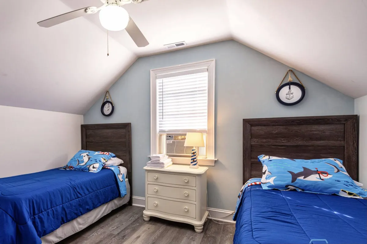 A playful twin bedroom with two themed beds, a nightstand with a lamp, and a window with blinds. The room is inviting and cheerful, designed for children or multiple guests, and offers a sense of privacy and fun.