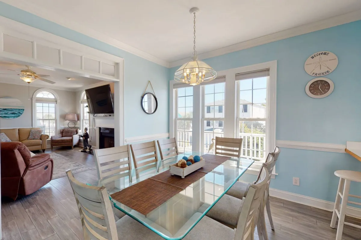 A comfortable dining area with a large table, blue accent wall, expansive windows, and a connected seating area. The setup is bright and inviting, designed for family meals, celebrations, and memorable group gatherings.