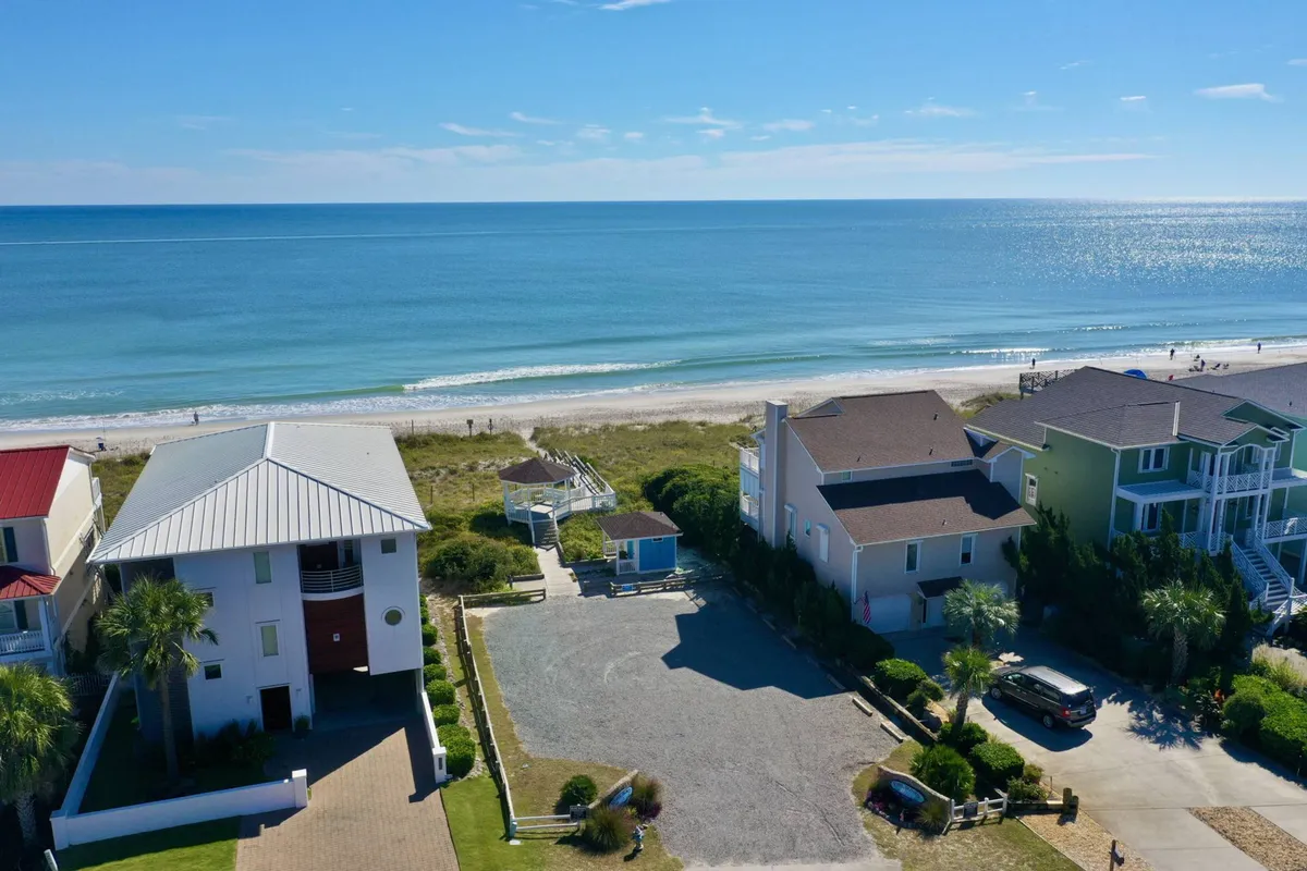 This exterior image showcases a sweeping view of the beach, with soft sand stretching toward the ocean and vacation homes nearby. The mood is relaxed, and the scene captures the essence of morning or sunset walks along the shore—activities ideal for guests and their dogs.